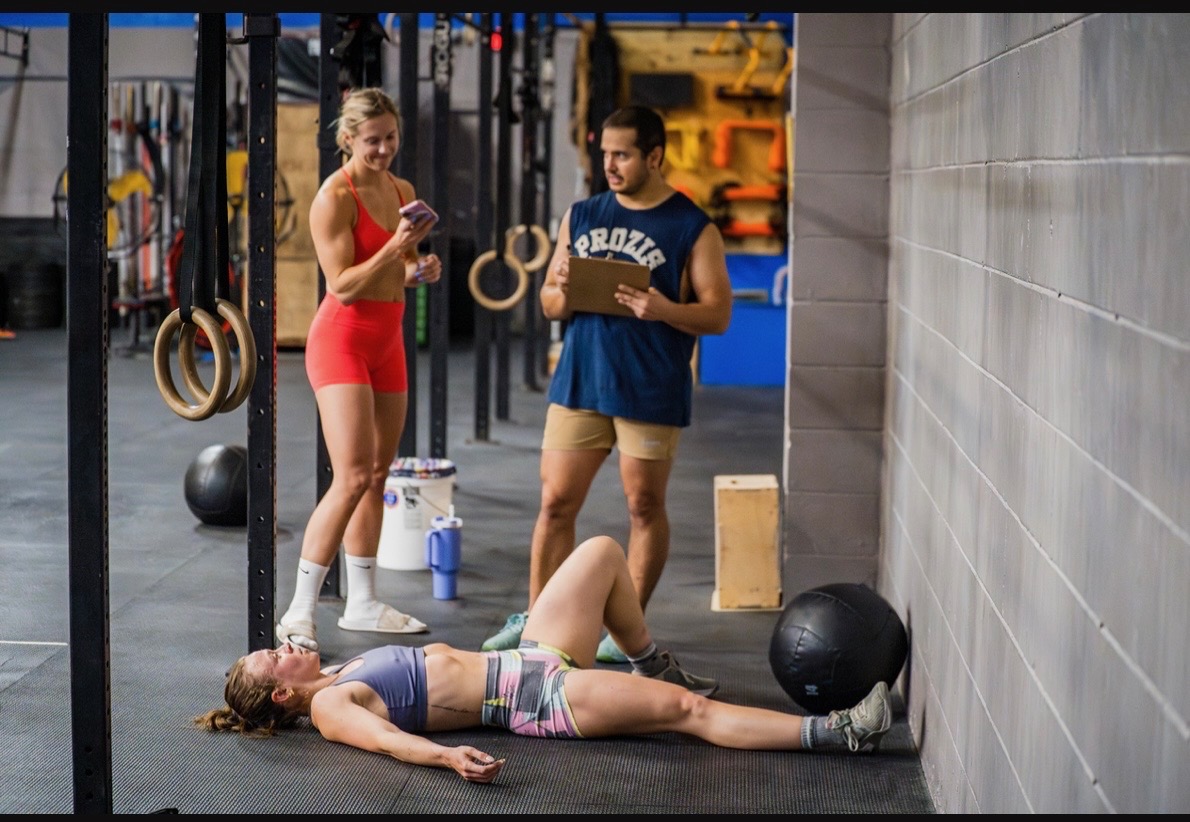 Jenna catching her breath on the floor between sets while coaches look on